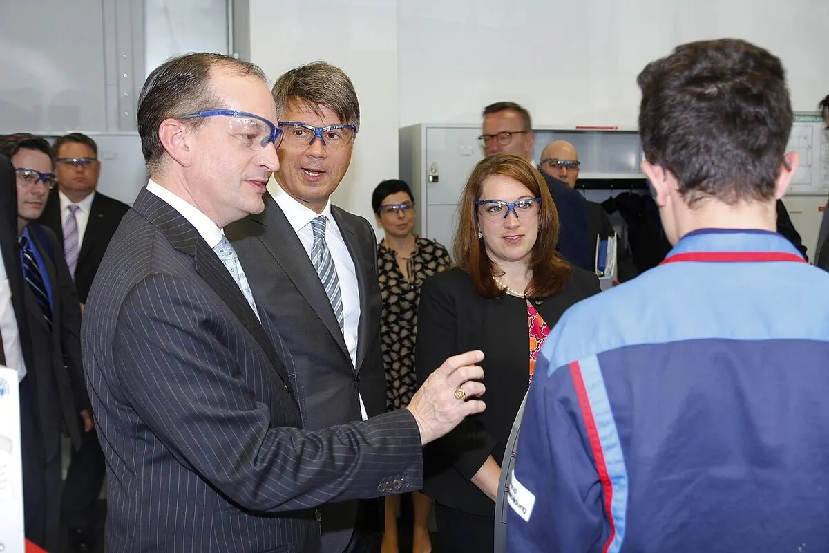 Trainee in a blue work jacket talking with visitors in a German company training workshop