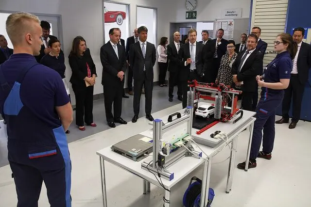 Visitors and trainees around a mechatronics teaching rig in a company workshop